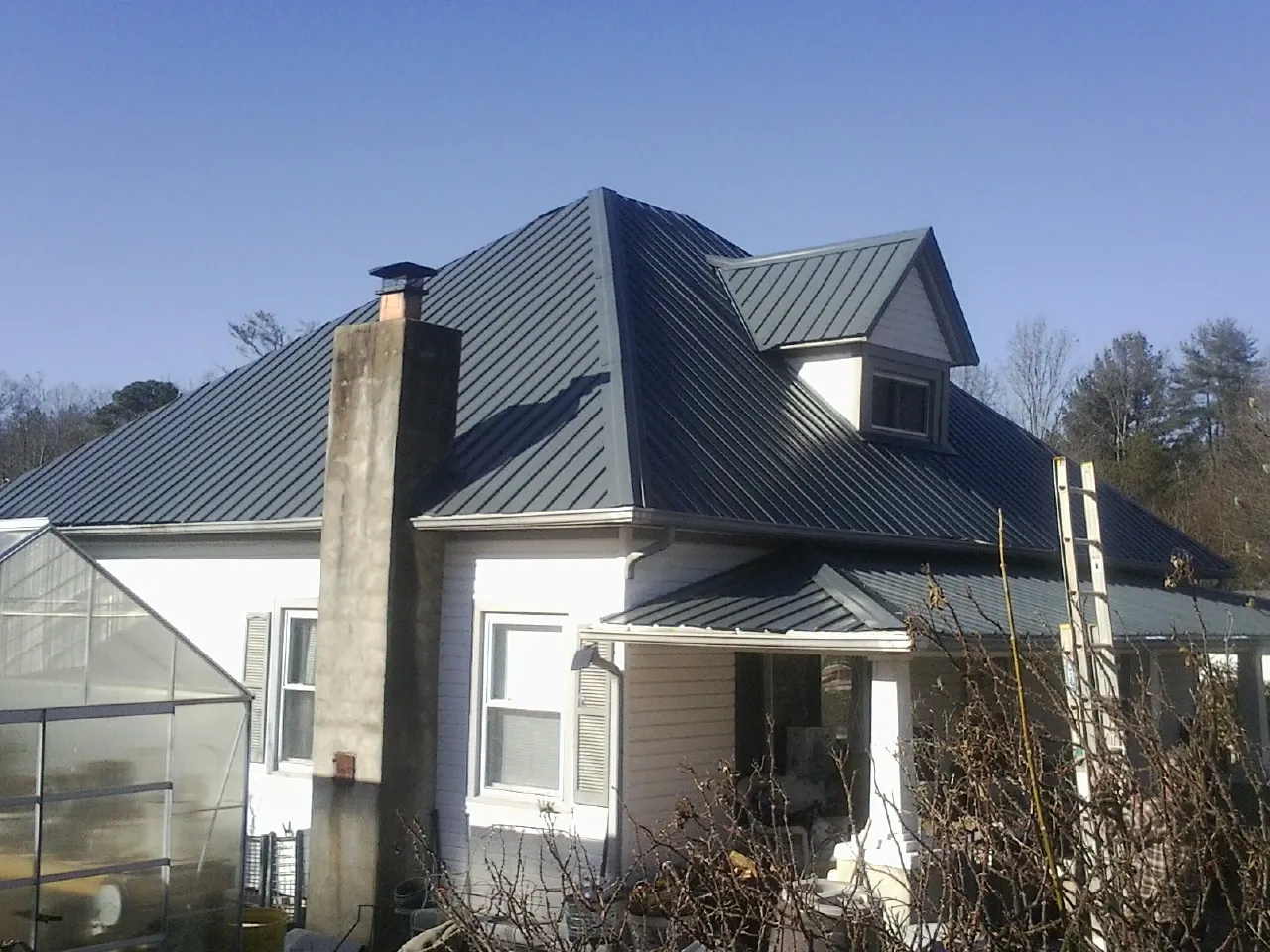 Dark blue standing seam metal roof on a white farmhouse with dormer — Slate & Tile Roof Repair by Roofing Brothers in Houghton