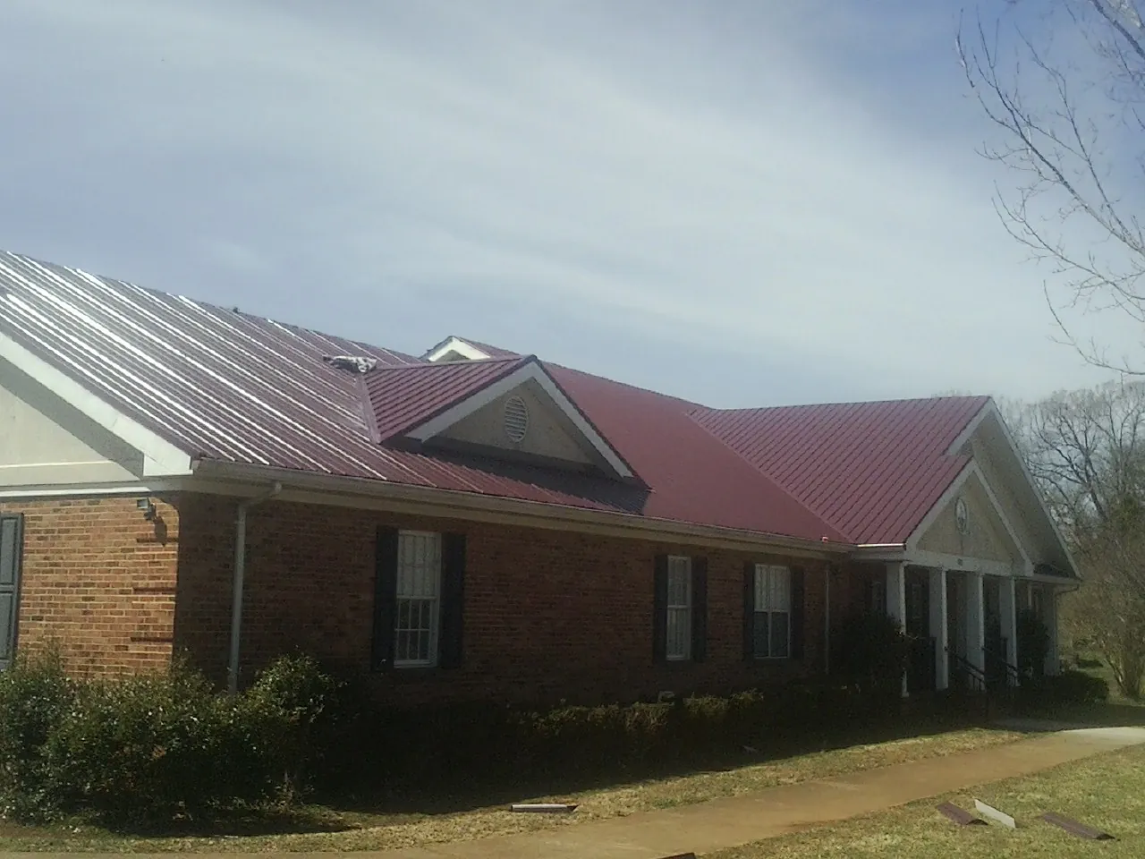 Red metal roof with gabled entries on a long brick building, from a Hail Damage Roof Repair job in Houghton