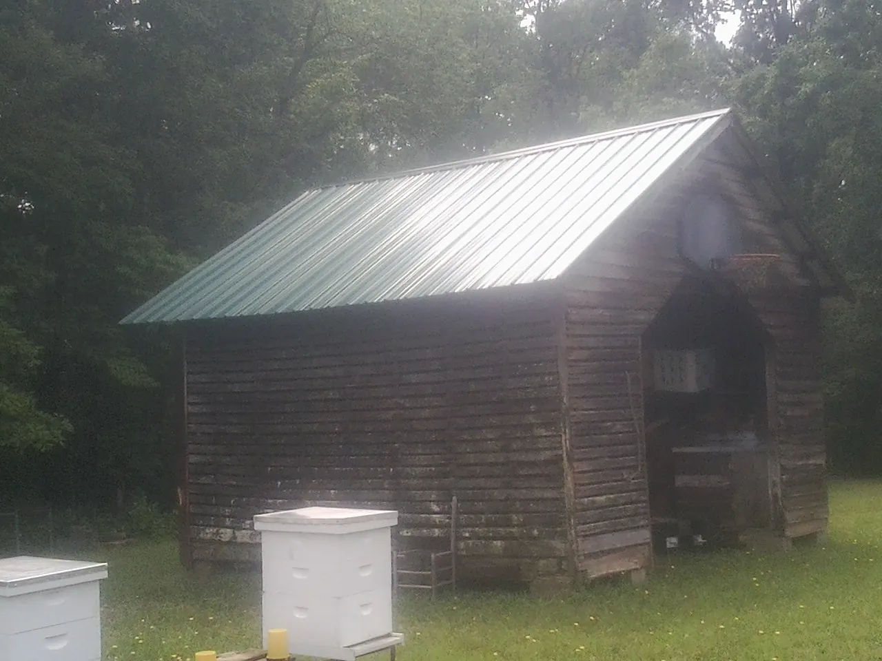 Green metal roof on a weathered barn beside stacked beehives in Houghton