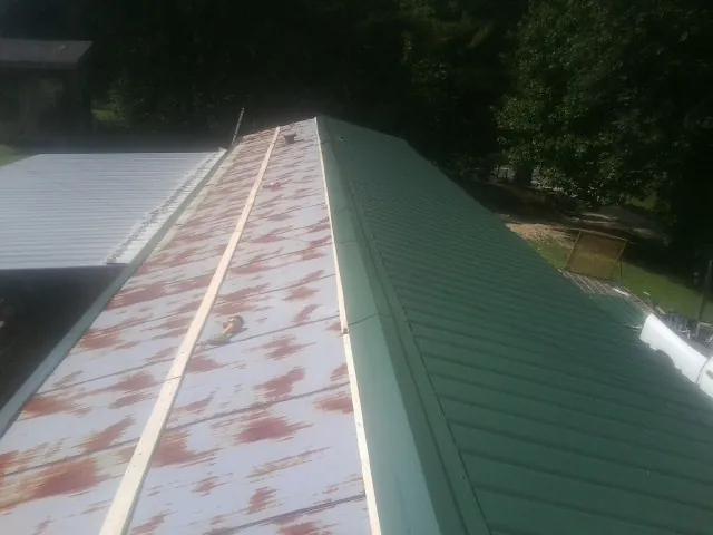 Old rusted panels beside newly installed green metal roofing — Wind Damage Roof Repair by Roofing Brothers in Houghton