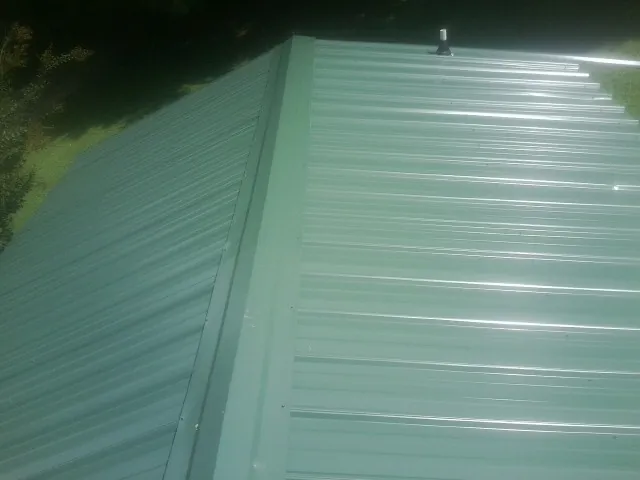 New green metal panels meeting at the ridge of a roof — Flat Roof Repair work by our crew in Houghton
