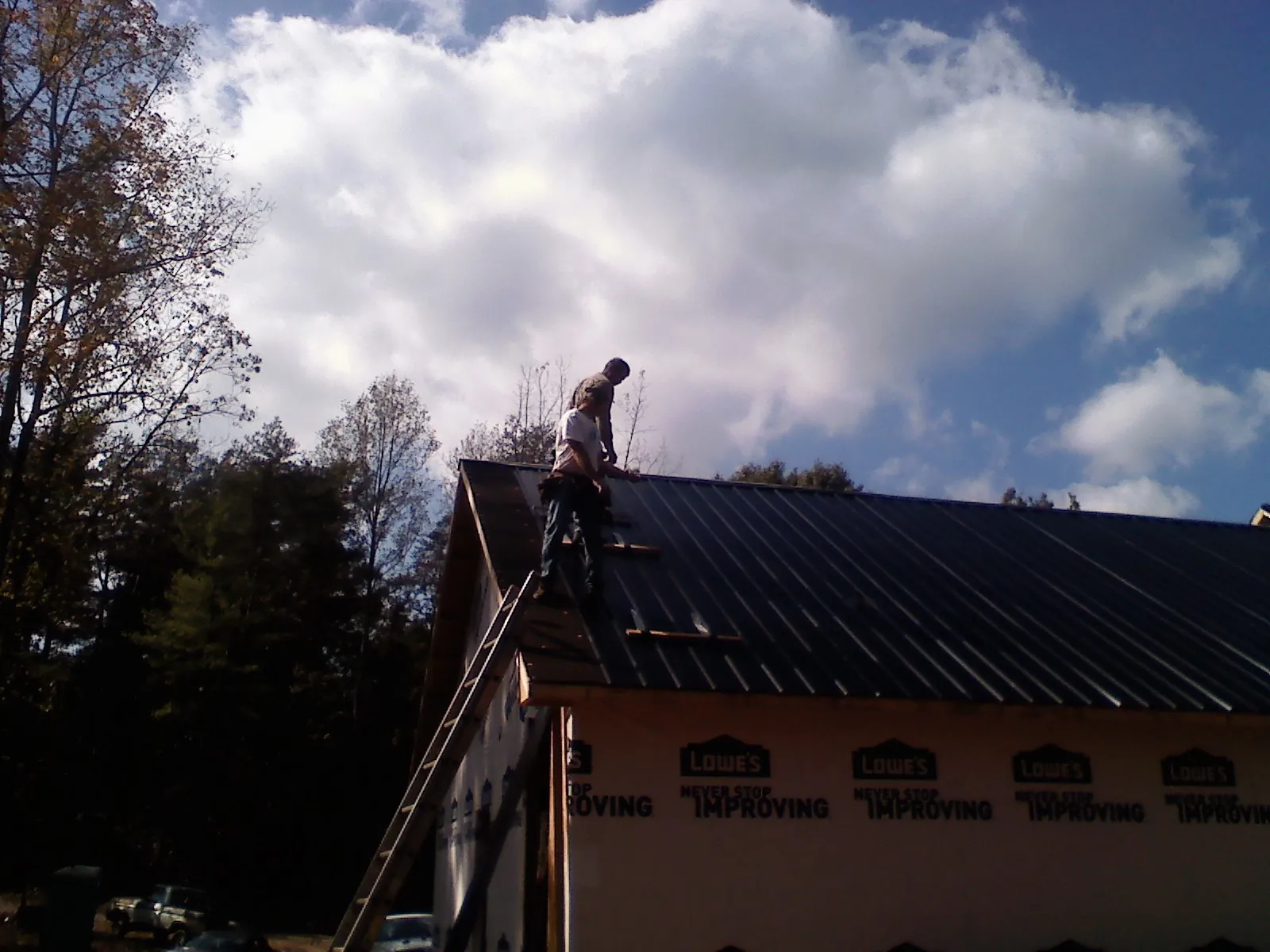 Roofer fastening dark metal panels high against a cloudy sky, from a Roof Inspection job in Houghton