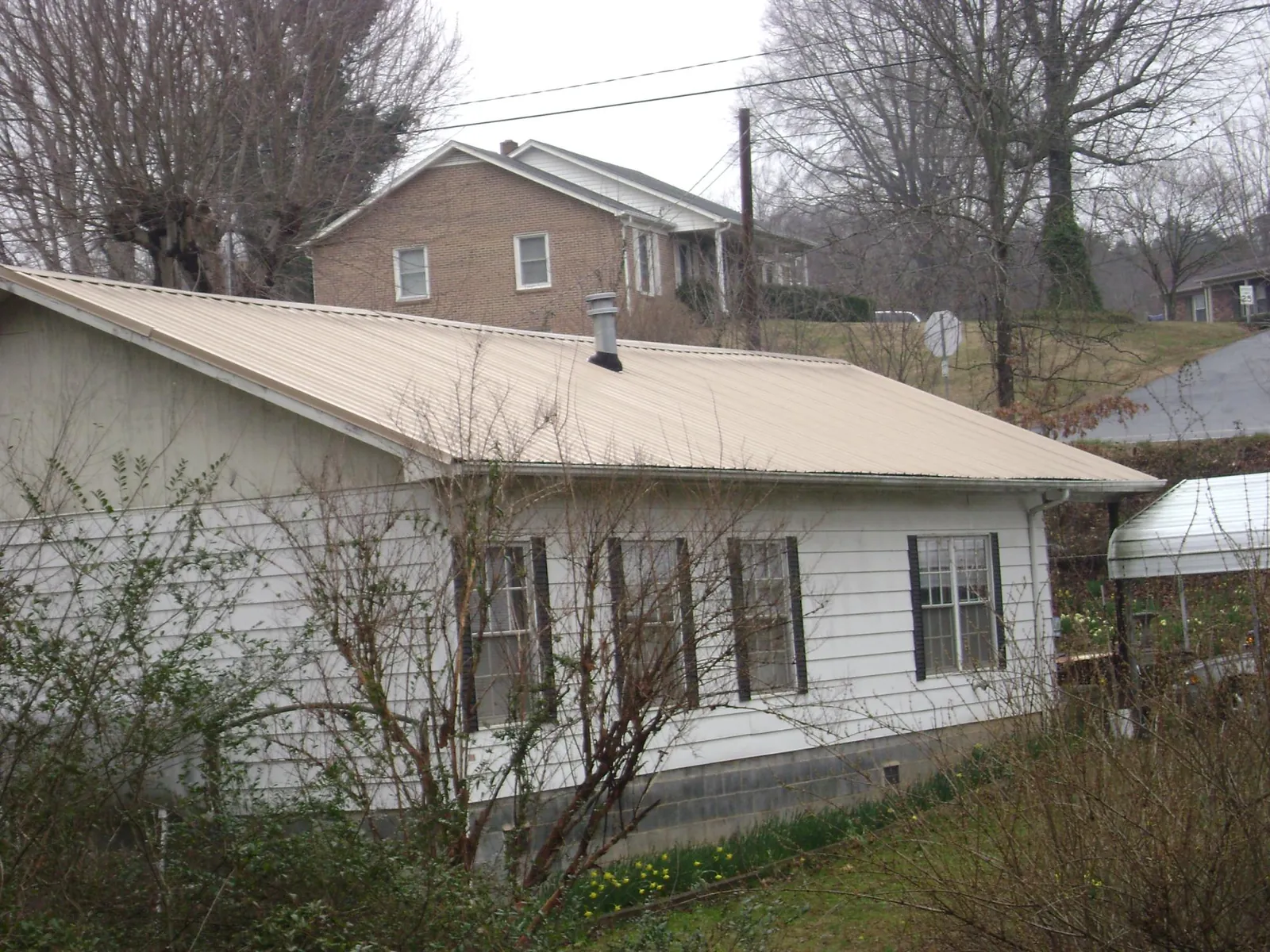 Tan metal roof on a white sided house set into a hillside — Commercial Roofing by Roofing Brothers in Houghton