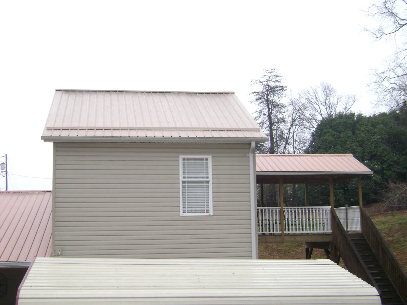 Tan metal roofs on a two story addition and attached porch, from a Roof Replacement job in Houghton